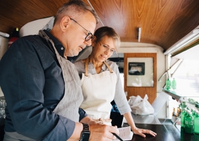 Mature owners looking at order while standing in food truck 